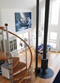 View from mezzanine down spiral staircase into double-height interior with central stovepipe and photo poster of sailing yacht