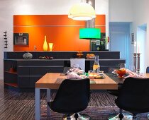 Black shell chairs around set table in front of kitchen island and orange fitted cupboards