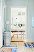 Wood-clad foyer in pastel blue with simple chest of drawers next to open doorway with view into rustic dining room