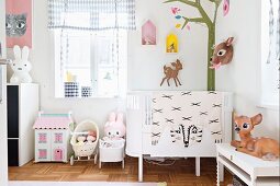 Cot in corner of room with mural of stylised tree and deer ornaments