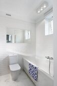 White designer bathroom; toilet with cistern against tiled wall, bathtub with marble surround and marble floor