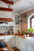 Küchenzeile mit Holz- Arbeitsplatte und weissen Unter- und Oberschränken im Landhausstil