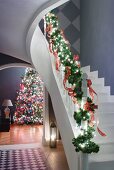 Staircase balustrade decorated with fir branches and view of decorated Christmas tree through arched doorway to one side
