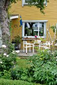 White garden furniture on terrace adjoining yellow-painted wooden house