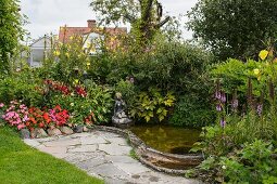 Flowering plants around small pond with stone figurine on edge next to small paved area