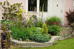 Flowering herbaceous border with stone surround against house façade