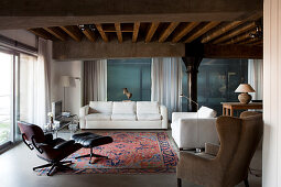 Loungebereich mit Klassiker Sessel und weiße, moderne Couchgarnitur in Loft-Wohnbereich mit rustikaler Holzbalkendecke