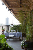 Table with black and white checked table cloth and potted plants on veranda with view of city