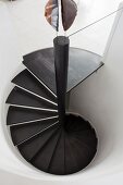 Spiral staircase with black wooden treads in white cylindrical stairwell