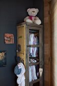 Vintage Schrank mit aufgehängter Mädchenkleidung und weißer Teddybär in grau getönter Zimmerecke