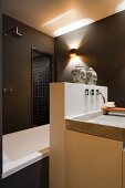 Designer-Waschtisch mit Vormauerung und zwei Buddhaköpfen vor Badewanne und Duschbereich in dunkelbraunem Bad