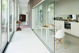 Narrow corridor with glass wall, dining set with classic, white chairs and modern kitchen counter