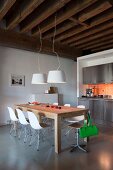 Stainless steel kitchen counter with orange wall tiles, rustic wood-beamed ceiling and wooden table with white designer chairs in loft apartment