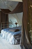 Double bed below wooden structure with casually draped canopy in attic bedroom