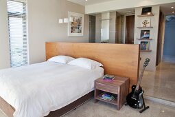E-Gitarre neben dem Nachtkästchen eines Doppelbetts, dahinter ein halbhoher Raumteiler mit Schreibplatz vor dem Bad Ensuite