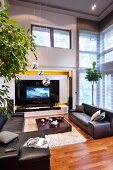 Black leather sofa set and low coffee table on flokati rug, TV in niche and transom window in high-ceilinged, elegant interior
