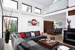 Black leather couch, dark wood and red accessories in double-height interior with mezzanine