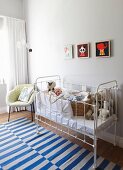 Flechtkorb mit Baby in weißem Vintage Gitterbett, Fifties Sessel und blau-weiss gestreifter Webteppich im Kinderzimmer