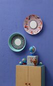 Old colander and steamer embroidered with colourful yarn and with small mirrors in centres decorating wall