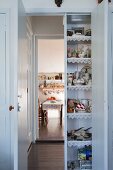 Kitchen utensils in cupboard built into doorway and open doors with view into dining room