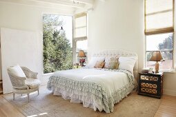 Bright bedroom with ruffled bedspread on double bed and open window with garden view