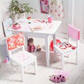 White, children's table and chairs painted with numbers and with patterned, fabric backrest covers