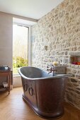 Vintage Metall-Badewanne vor Natursteinwand in renoviertem Bad mit Fenster