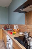Küchenzeile mit Arbeitsplatte und Schrankfronten aus Holz, an hellblau getönter Wand