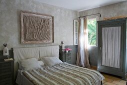 Double bed with striped bedspread and wardrobe with gathered fabric door panel in bedroom in natural shades