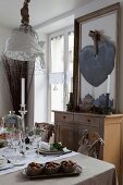 Gedeckter Tisch unter dekorierter Maschendraht-Pendelleuchte und Flohmarkt-Kommode mit Dekoherz auf gerahmtem Spiegel