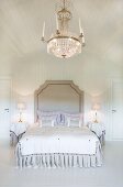 Opulent crystal chandelier above grand double bed in white-panelled bedroom