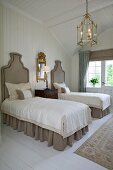 Twin beds with upholstered headboards, brass light fitting and gilt-framed mirror in wood-panelled bedroom
