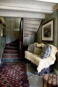 Cushions and pale fur blanket on bench next to rug at foot of winding wooden staircase in rustic foyer