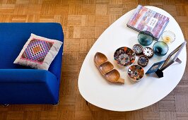 Various bowls on retro coffee table with white top next to blue easy chair on mosaic parquet floor