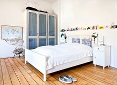 White double bed with headboard, glass-fronted cabinet and wooden floor in rustic bedroom with vintage ambiance