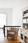 Ecru armchair against wooden landing balustrade and vintage-style white dresser on rustic gallery
