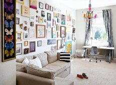 Beige corner sofa below large gallery of pictures on wall; desk below window with floor-length, black and white striped curtains