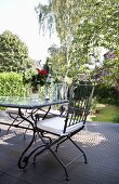 Metal chair with white seat cushion at outdoor table on wooden terrace in sunny garden