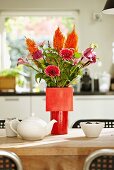 Blumenstrauss aus Gerbera und Calla in verschiedenen Rottönen in roter Vase auf Esstisch