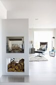 Gemauerter Kamin in offenem Wohnraum mit minimalistischem Flair, im Hintergrund Lounge Sessel mit Fussschemel