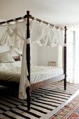 Antique four-poster bed with turned bedposts and white, draped fabric in Mediterranean interior