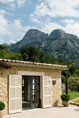 Mediterranean stone house with open terrace doors and pale shutters against mountain landscape