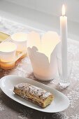 Take-away carton, tealights in paper cups, lit candle in glass and Swiss roll