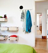 Bed with green bedspread, wooden boxes mounted on wall and scarves hanging from hooks next to open door