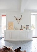 White, custom-made sideboard, framed pictures and hunting trophy in minimalist country-house interior with wooden floor