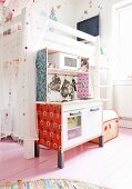Child's bedroom with tulle curtains on white loft bed, pale wooden floor and patterned wallpaper