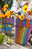 Yellow cut flowers in terracotta plant pots brightly painted by children