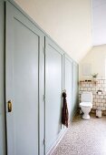 Fitted cupboards with grey-painted doors and pedestal toilet on terrazzo floor