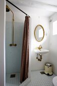 Abgetrennter Duschbereich mit braunem Vorhang, seitlich Waschbereich, ovaler Spiegel mit Goldrahmen an Wand