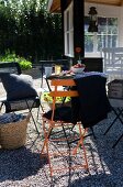 Blanket and cushions on colourful folding chairs on gravel terrace in garden